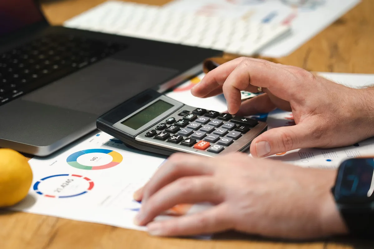 Person calculating average order value on a laptop next to a printed sales report