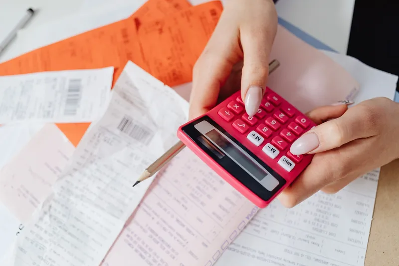 Close-up of hands using a calculator alongside printed order receipts