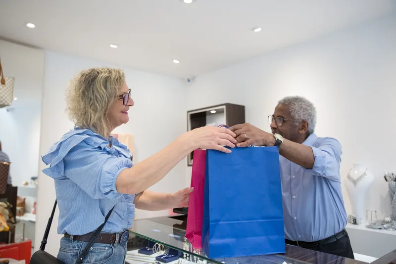 Two people exchanging blue and pink shopping bags across a glass counter in a boutique