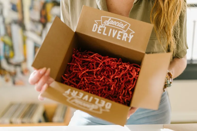Person opening a cardboard box marked Special Delivery and filled with red shredded paper