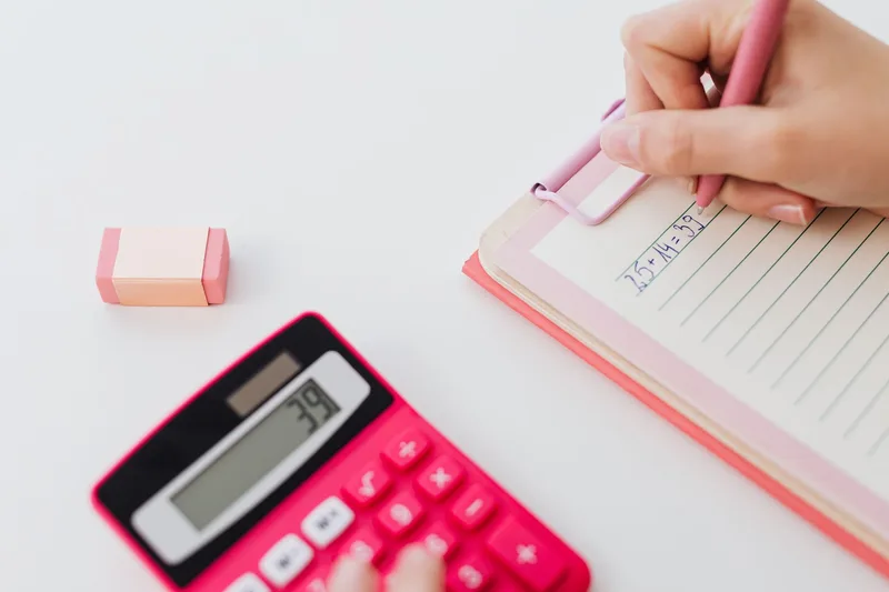 Hands using a calculator and writing figures in a notebook