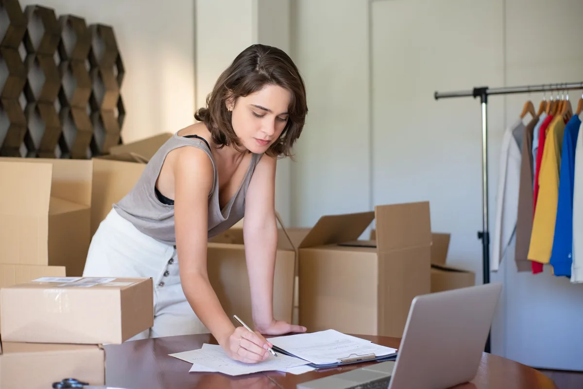 Young woman managing her online clothing business from a home office with boxes and a laptop